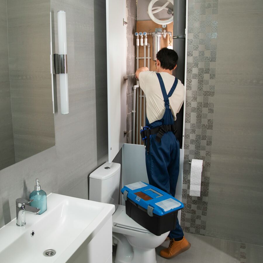 Plumber installing pipework behind a bathroom wall